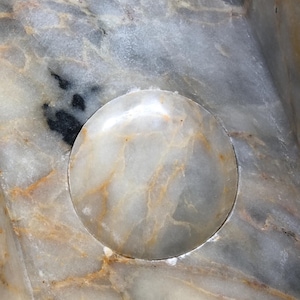 May include: A close-up of a white marble surface with a circular indentation. The indentation is smooth and polished, and the marble has a subtle veining pattern.