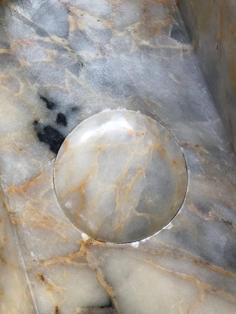 May include: A close-up of a white marble surface with a circular indentation. The indentation is smooth and polished, and the marble has a subtle veining pattern.
