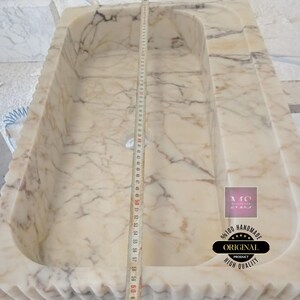May include: A white marble sink with a wavy edge and a drain hole. The sink is 60 inches long and is handmade. The text "100% HANDMADE ORIGINAL PRODUCT HIGH QUALITY" is visible in the image.