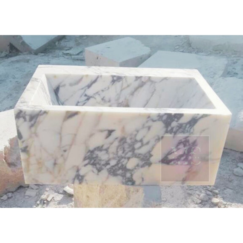 May include: A white marble sink with a rectangular shape and a smooth, polished surface. The sink has a subtle veining pattern in shades of gray and pink.