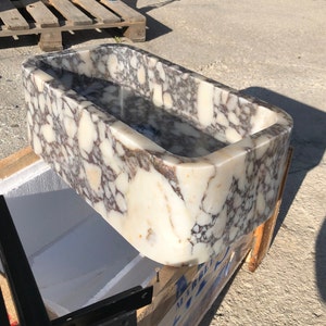 marble bathroom sink with premium natural stone veining, handcrafted from solid Carrara marble with a 6-inch rounded backsplash. Wall-mounted or countertop installation, modern minimalist luxury bathroom design. High-end 3-hole faucet installed, polished surface, durable natural stone craftsmanship. Perfect for luxury interior design projects, small bathrooms, powder rooms, hotels, and modern home renovations. Premium quality, handcrafted marble vanity sink shipped worldwide via DHL Express.
