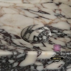 Puede incluir: Primer plano de un lavabo de m&aacute;rmol blanco con una tapa de desag&uuml;e redonda de m&aacute;rmol blanco. El lavabo tiene un patr&oacute;n de vetas grises y moradas en espiral. El texto "100% HANDMADE ORIGINAL PRODUCT HIGH QUALITY" es visible en la esquina inferior derecha de la imagen.
