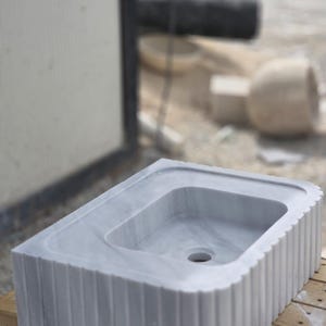 Elegant marble countertop sink placed on wood vanity showing natural veining and custom carved edges handmade stone basin