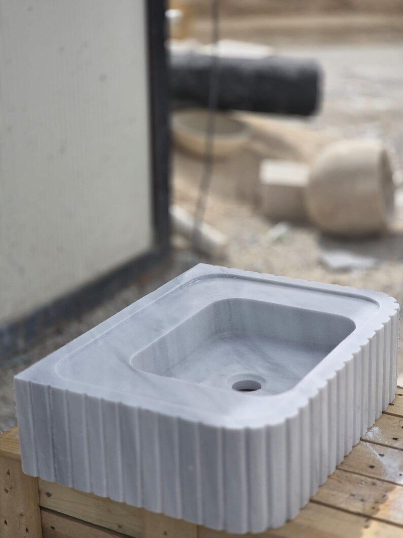 Elegant marble countertop sink placed on wood vanity showing natural veining and custom carved edges handmade stone basin