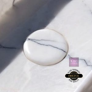 Puede incluir: Un jabonera redonda de m&aacute;rmol blanco con un sutil patr&oacute;n de vetas. La jabonera est&aacute; sobre una superficie de m&aacute;rmol blanco.