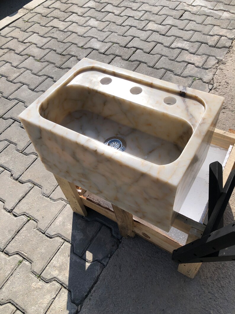 High-angle front view of a handmade Calacatta Viola marble washbasin with a thick stone apron, rounded rectangular bowl, centered drain and three deck-mount faucet openings.