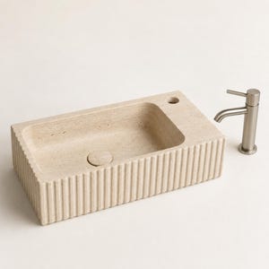 Hand-carved beige travertine sink with ribbed exterior, centered drain and right faucet hole