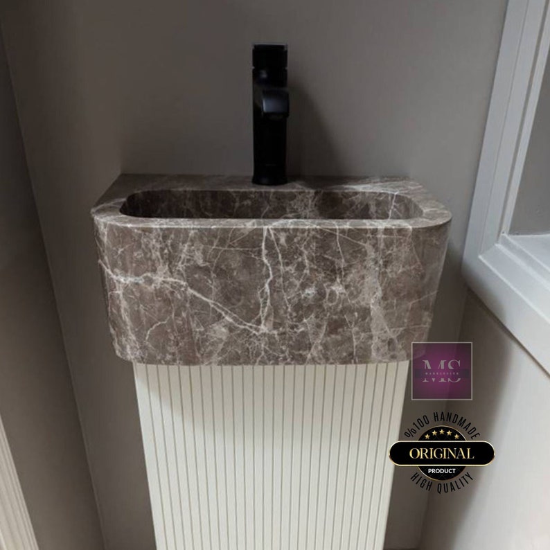 May include: A brown marble bathroom sink with a black faucet. The sink is mounted on a white pedestal with vertical grooves. The sink is labeled "100% Handmade Original Product High Quality".