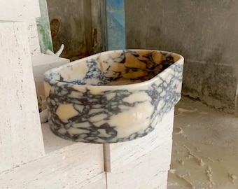May include: A white and black marble oval sink with a textured surface.