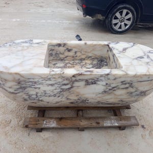 Calacatta Viola suspended marble sink, luxury floating vanity sink hand carved from a 2 ton marble block, rare sculptural bathroom basin designed for luxury villas, penthouses and designer interiors, architectural statement sink suspended with steel chains creating a dramatic floating illusion, premium handmade marble sink crafted by MarbleSinkCo masters, collectible luxury bathroom centerpiece shipped worldwide with DHL Express