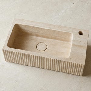 Top view of fluted travertine bathroom sink showing centered drain and right-side faucet hole