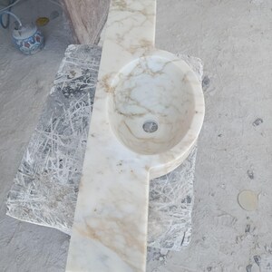 Luxurious wall-mounted Calacatta marble sink carved from a single block. Featuring 3 faucet holes, fluted front design, and floating vanity look. Ideal for modern, minimalist bathrooms. Custom sizes available. Handmade from natural Italian stone. Bathroom sink, marble vanity, stone basin, designer sink, fluted marble, wall mount sink, handmade sink, rectangular sink, luxury bathroom decor.