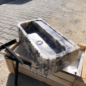 Close angled view of the long rectangular stone basin showing its polished bowl, drain and naturally varied marble veins.