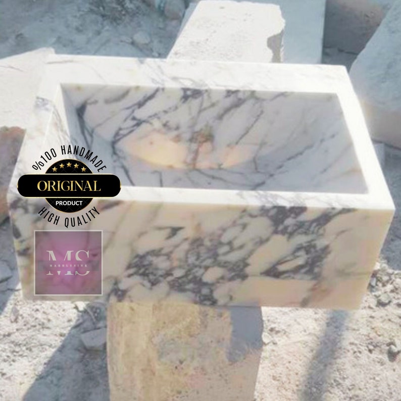 May include: A white marble sink with gray veining. The sink is handmade and has a rectangular shape. The sink is sitting on a white marble base.