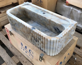 May include: A white marble sink with a fluted design. The sink is in a wooden crate with the text "MC MARBLESINK" printed on the side.