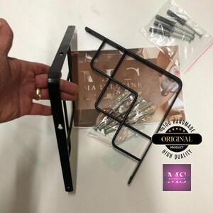 Puede incluir: Estanter&iacute;a de metal negro con un dise&ntilde;o geom&eacute;trico. La estanter&iacute;a est&aacute; hecha de dos piezas que se conectan entre s&iacute;. La estanter&iacute;a est&aacute; etiquetada como "Producto original, Alta calidad, Hecho a mano".