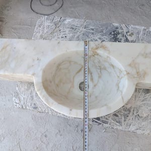 Luxurious wall-mounted Calacatta marble sink carved from a single block. Featuring 3 faucet holes, fluted front design, and floating vanity look. Ideal for modern, minimalist bathrooms. Custom sizes available. Handmade from natural Italian stone. Bathroom sink, marble vanity, stone basin, designer sink, fluted marble, wall mount sink, handmade sink, rectangular sink, luxury bathroom decor.