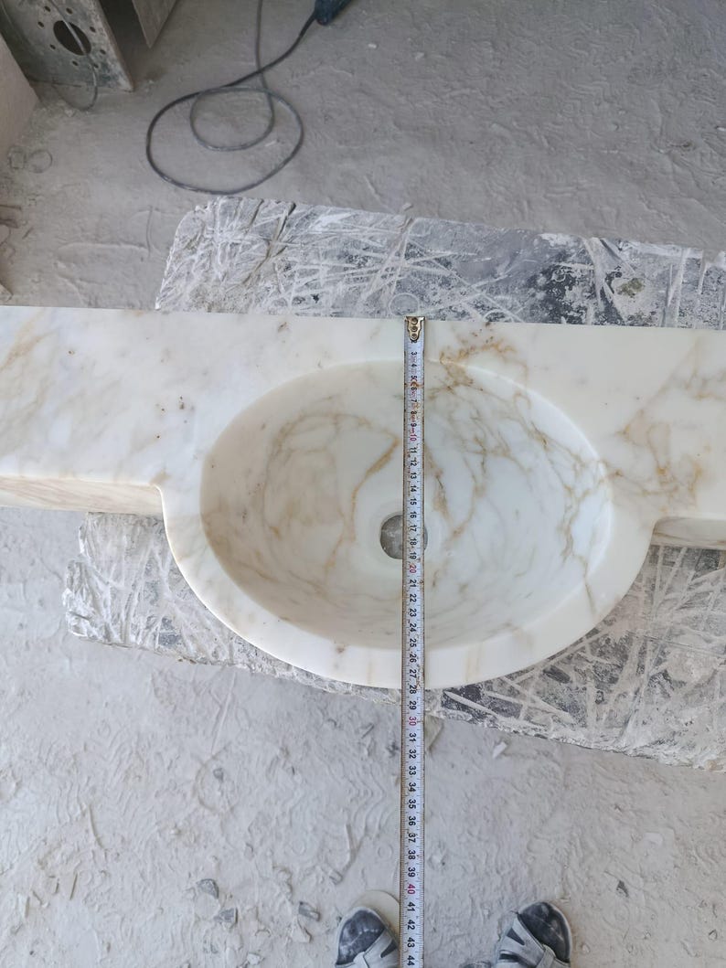 Luxurious wall-mounted Calacatta marble sink carved from a single block. Featuring 3 faucet holes, fluted front design, and floating vanity look. Ideal for modern, minimalist bathrooms. Custom sizes available. Handmade from natural Italian stone. Bathroom sink, marble vanity, stone basin, designer sink, fluted marble, wall mount sink, handmade sink, rectangular sink, luxury bathroom decor.