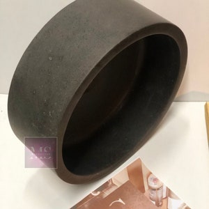Pu&ograve; includere: Un vaso rotondo in ceramica di colore marrone scuro con una superficie ruvida e testurizzata.