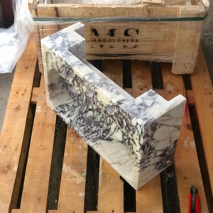 Puede incluir: Un lavabo de m&aacute;rmol blanco con vetas moradas y grises. El lavabo est&aacute; montado en una tarima de madera. El lavabo est&aacute; etiquetado con "MC MARBLESINK".