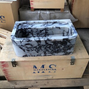 May include: A white marble sink with purple veining, in a wooden crate with the text "MC MARBLESINK" printed on the side.