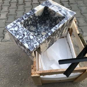 May include: A white marble sink with black and brown veining. The sink is in a wooden crate with white foam padding.