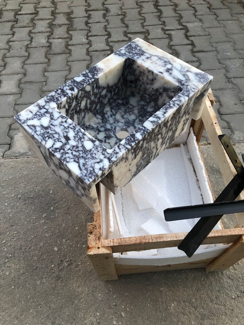 May include: A white marble sink with black and brown veining. The sink is in a wooden crate with white foam padding.