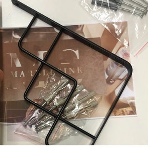 Puede incluir: Soporte de estante de metal negro con un dise&ntilde;o geom&eacute;trico. El soporte est&aacute; fijado a una pared con tornillos y anclajes. El soporte de estante est&aacute; dise&ntilde;ado para sostener un estante u otros art&iacute;culos.
