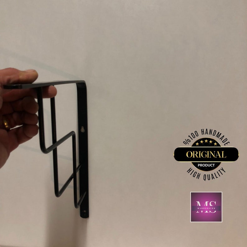 Puede incluir: Estante de vino de pared de metal negro con tres niveles. El estante est&aacute; fijado a una pared blanca. La imagen incluye una superposici&oacute;n de texto que dice "100% Hecho a Mano Producto Original Alta Calidad" y un logotipo que dice "MC Manufacturing".