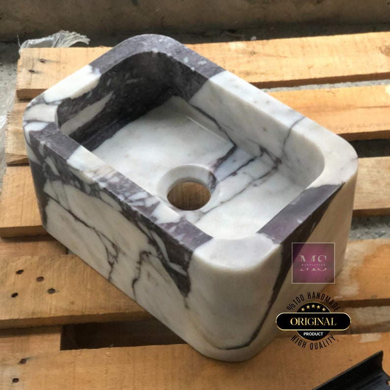 Three-quarter view of a Calacatta Viola stone basin with an open drain hole and dramatic purple veining across the white marble.