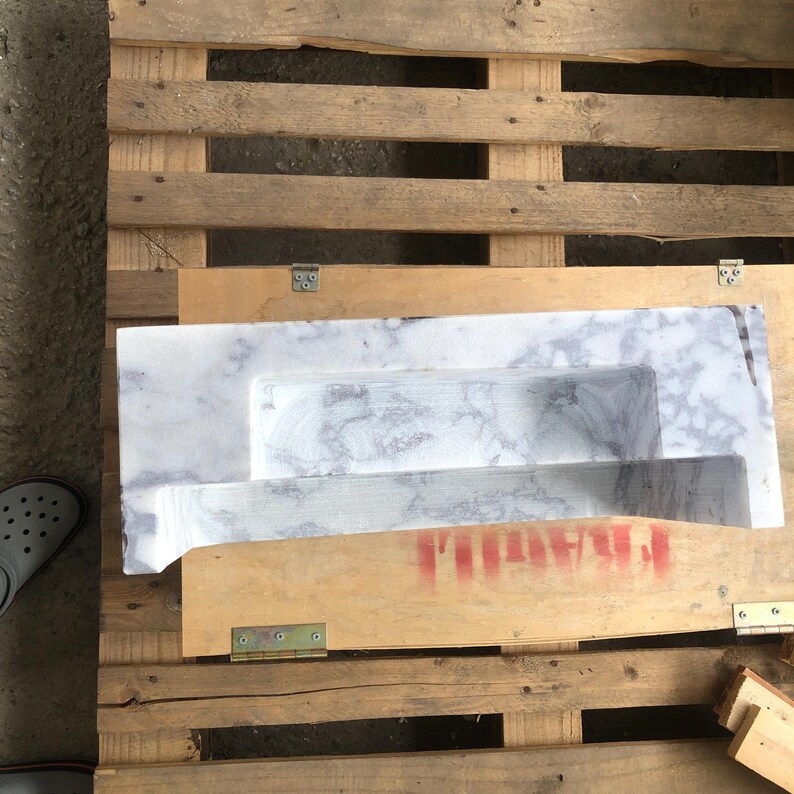 May include: A white marble sink with a unique design, resting on a wooden pallet.