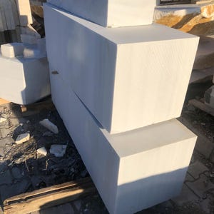 May include: Three white marble blocks stacked on top of each other. The blocks are rectangular and have a smooth, polished surface.