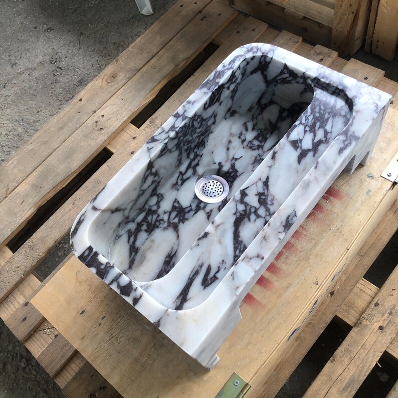 May include: A white marble sink with a black and purple marbling pattern. The sink has a single drain and is set on a wooden pallet.