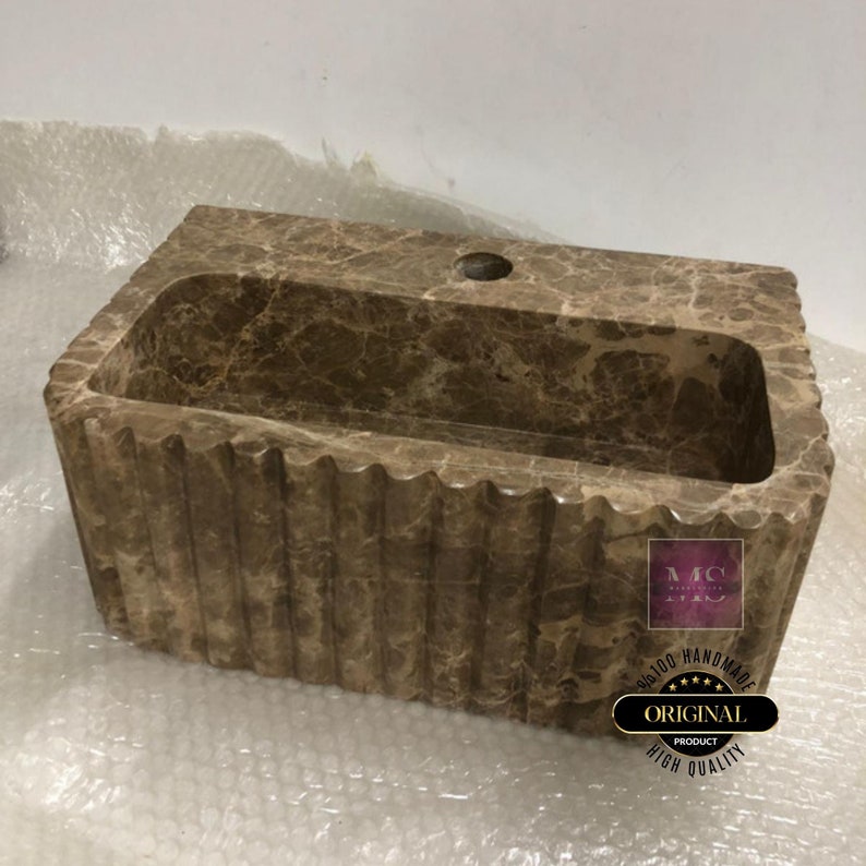 May include: A brown marble bathroom sink with a rectangular shape and a wavy edge. The sink has a single hole for a faucet and is made of natural stone. The sink is handmade and has a high quality finish.