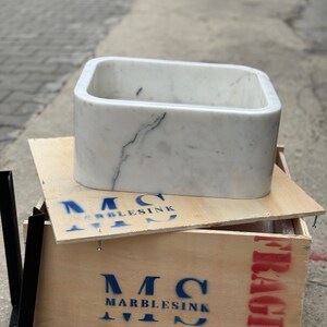 Straight front view of a solid Carrara White marble bathroom basin highlighting the thick polished apron, softly rounded corners and distinctive grey marble vein.