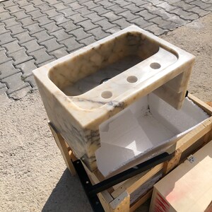 Rear three-quarter view of the Calacatta Viola marble sink showing the open wall side, thick stone edges, carved basin, three faucet holes and underside space prepared for wall mounting.