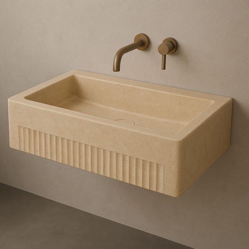 Handmade travertine wall-mounted sink with fluted front and matte finish. Custom sizes available. Ideal for luxury bathrooms, hotels, interior designers, and modern spa spaces. Each basin is carved from solid stone. Ships globally in a wooden crate via DHL Express. Natural veining varies uniquely in each piece.Perfect for minimalist,rustic,and architectural interiors, travertine wall-mounted sink,fluted front, solid stone, custom sizes,interior designers, modern spa, luxury bathrooms, minimalist