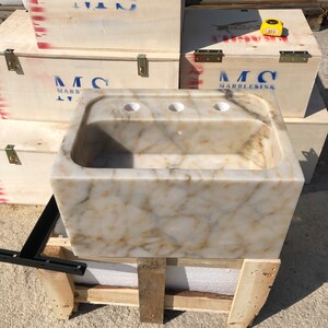 Straight front workshop view of a handmade Calacatta Viola marble sink, showing the thick polished front apron, natural cream and gold veining, deep basin and three faucet holes.