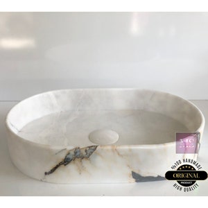May include: White oval marble bathroom sink with a drain hole and a light brown and gray marbling pattern. The sink is handmade and has a high quality finish.