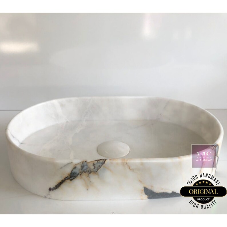 May include: White oval marble bathroom sink with a drain hole and a light brown and gray marbling pattern. The sink is handmade and has a high quality finish.