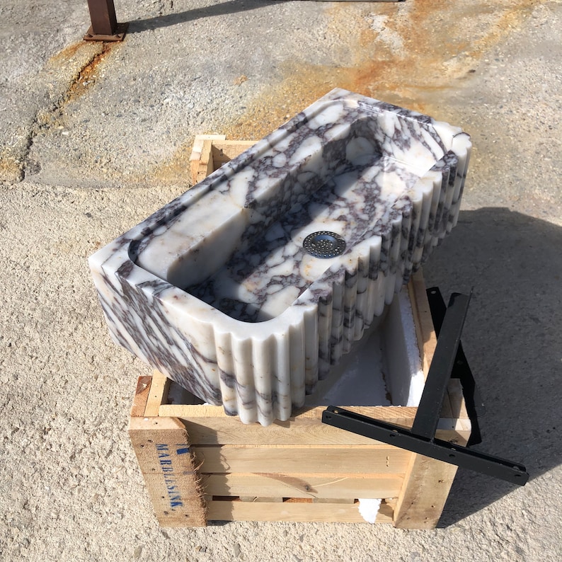 ```text
Angled overhead view of the Calacatta Viola wall-mounted sink showing its deep bowl, natural purple veining and metal brackets.
