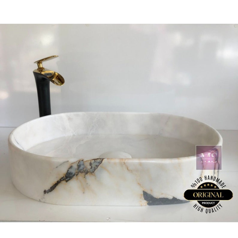 May include: White oval marble sink with gold faucet and a black base. The sink has a unique marbled pattern with gold and black accents. The sink is handmade and features the text "100% Handmade Original Product High Quality".