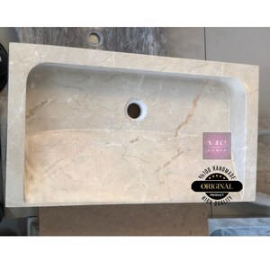 May include: A beige marble sink with a curved edge and a drain hole. The sink is handmade and has a high quality finish.