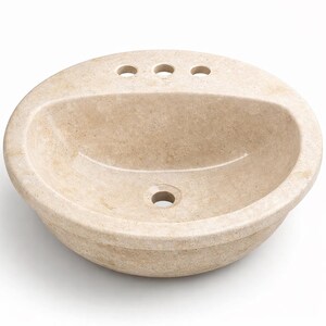 May include: A beige, oval-shaped bathroom sink made of stone. The sink has a rounded basin with three faucet holes and a single drain hole. The stone has a natural, textured appearance.