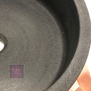 Pu&ograve; includere: Un lavandino rotondo in ceramica nera con una texture ruvida. Il lavandino ha un piccolo foro al centro.