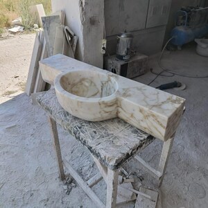 Luxurious wall-mounted Calacatta marble sink carved from a single block. Featuring 3 faucet holes, fluted front design, and floating vanity look. Ideal for modern, minimalist bathrooms. Custom sizes available. Handmade from natural Italian stone. Bathroom sink, marble vanity, stone basin, designer sink, fluted marble, wall mount sink, handmade sink, rectangular sink, luxury bathroom decor.