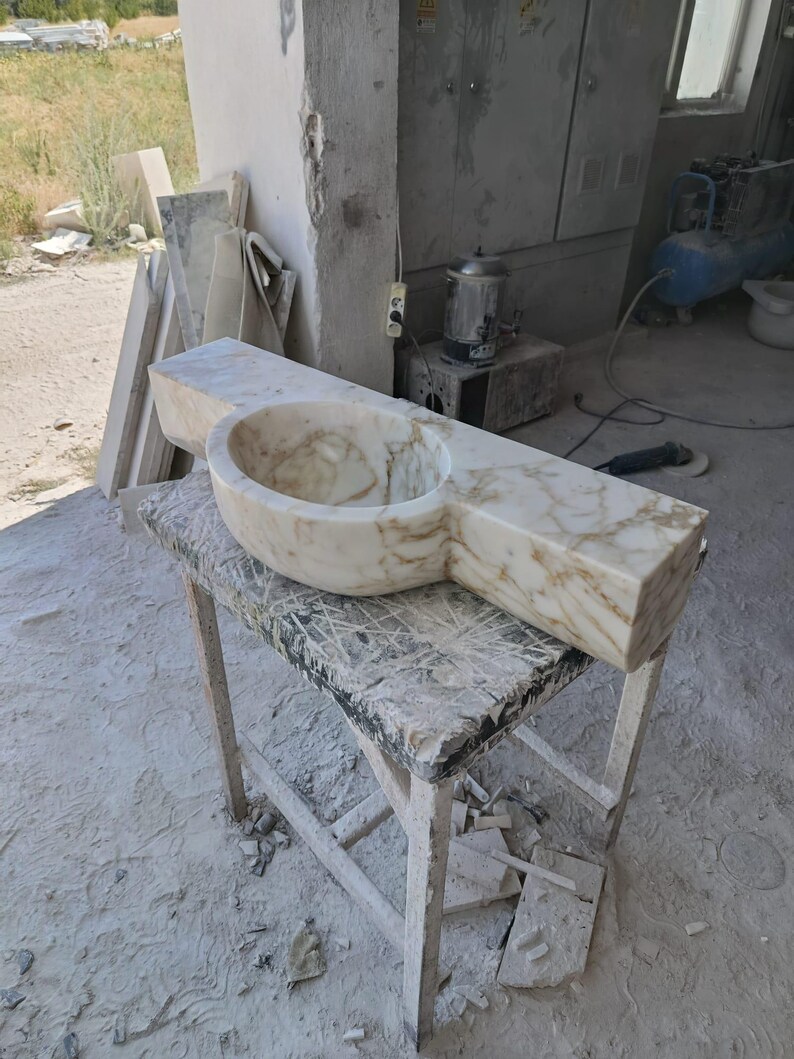 Luxurious wall-mounted Calacatta marble sink carved from a single block. Featuring 3 faucet holes, fluted front design, and floating vanity look. Ideal for modern, minimalist bathrooms. Custom sizes available. Handmade from natural Italian stone. Bathroom sink, marble vanity, stone basin, designer sink, fluted marble, wall mount sink, handmade sink, rectangular sink, luxury bathroom decor.
