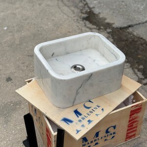 Left three-quarter view of a hand-carved Carrara marble countertop basin with a white background, natural grey veins, deep rectangular bowl and polished finish.