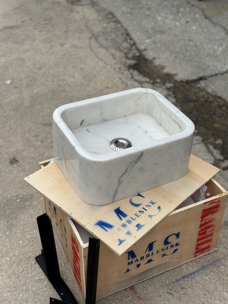 Left three-quarter view of a hand-carved Carrara marble countertop basin with a white background, natural grey veins, deep rectangular bowl and polished finish.