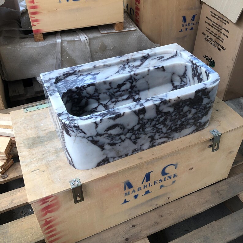 May include: A white marble sink with gray veining, sitting in a wooden crate with the text "MC MARBLESINK" printed on the side.